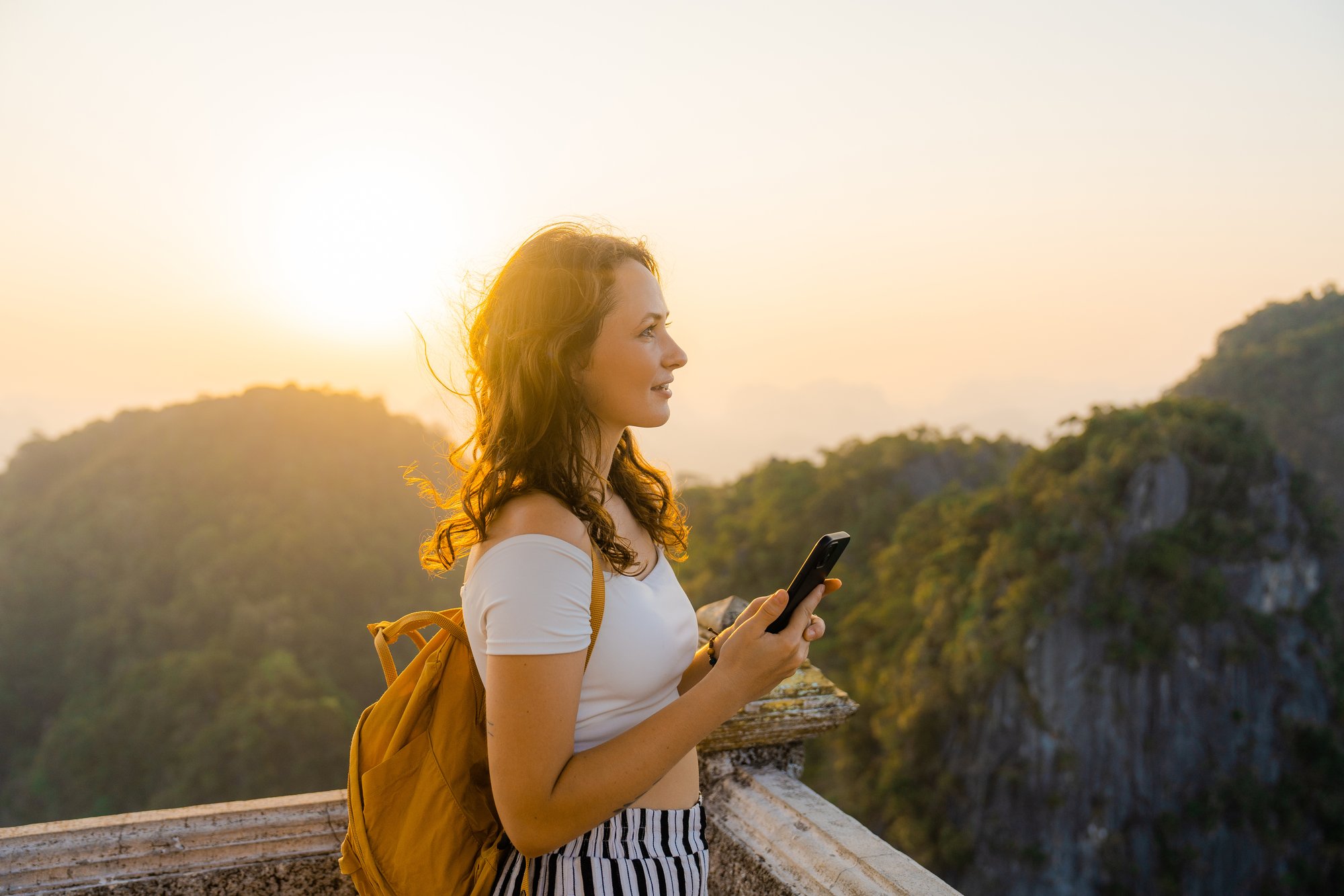 Young female traveler enjoying a view of the mountains with smartphone